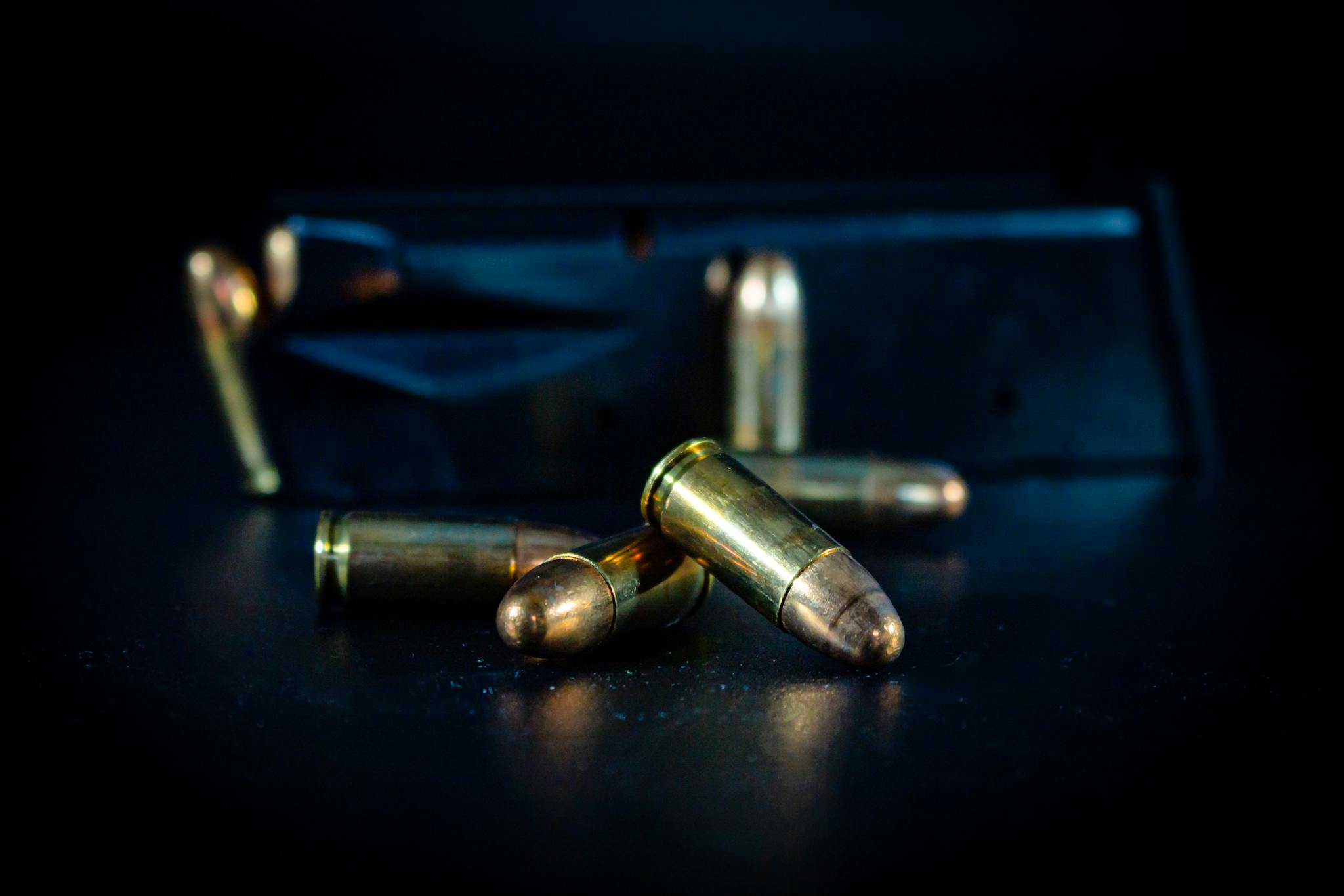 A macro shot of bullets and a gun magazine on a dark surface, highlighting the metallic texture.