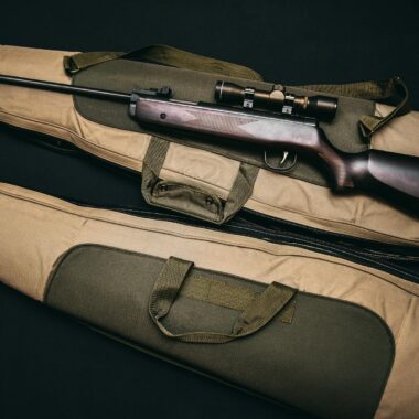 Close-up of a hunting rifle with a scope on a carrying bag, showcasing firearms and hunting gear.