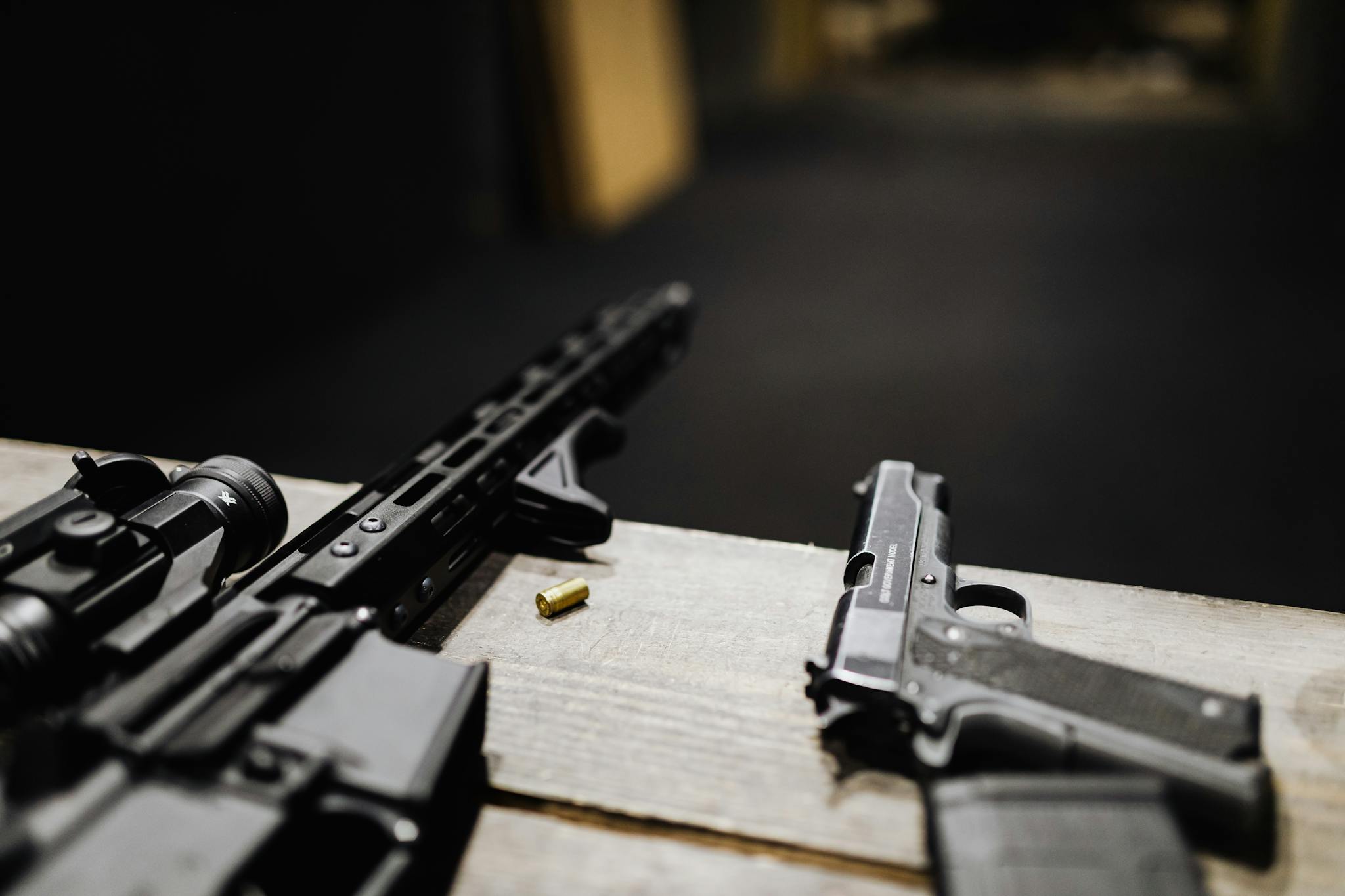 Detailed view of a rifle and handgun on a table at an indoor shooting range.
